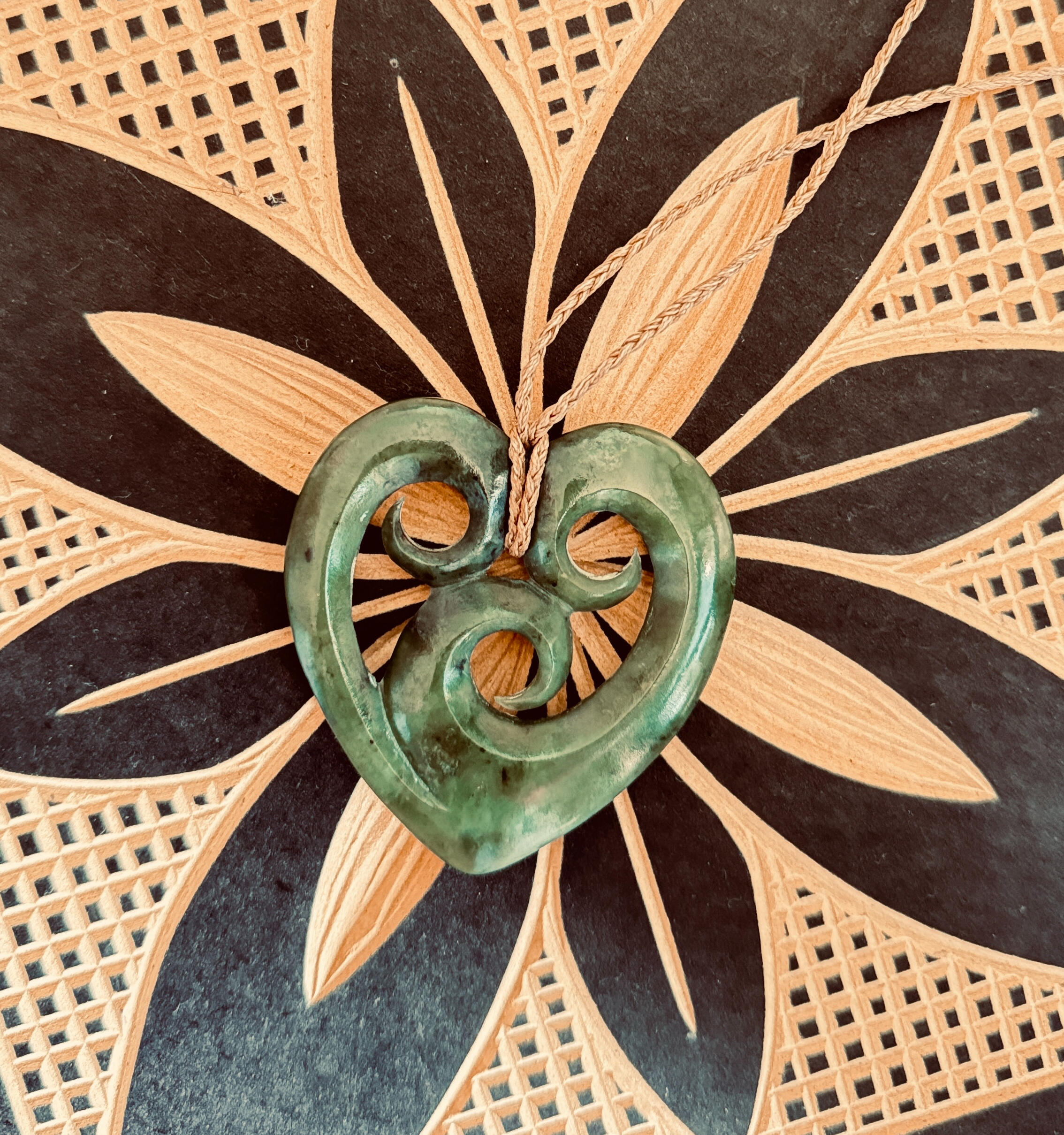 Image of a heart shaped pounamu taonga lying over a Samoan carving representing family.